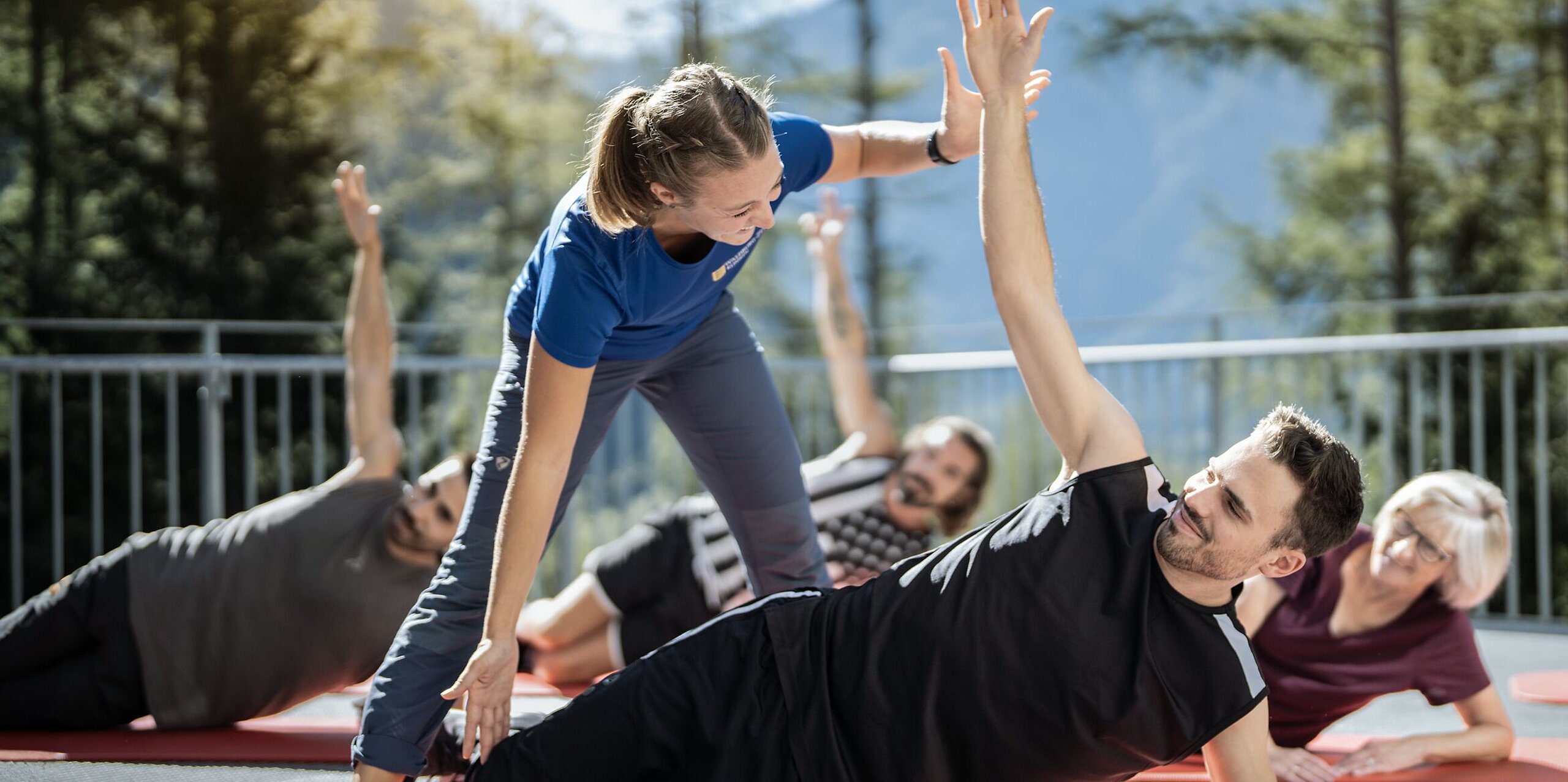Eine Trainerin korrigiert einen Mann der in einer seitlichen Yogapose ist auf einer roten Matte