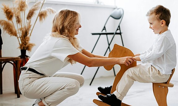 Eine freundliche Ärztin hält die Hände eines Jungen auf einem Schaukelpferd.