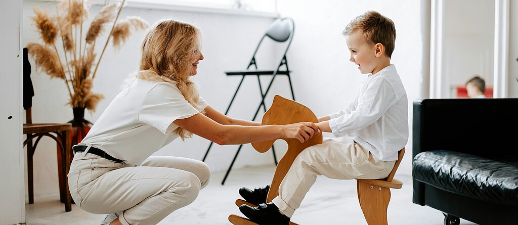 Eine freundliche Ärztin hält die Hände eines Jungen auf einem Schaukelpferd.