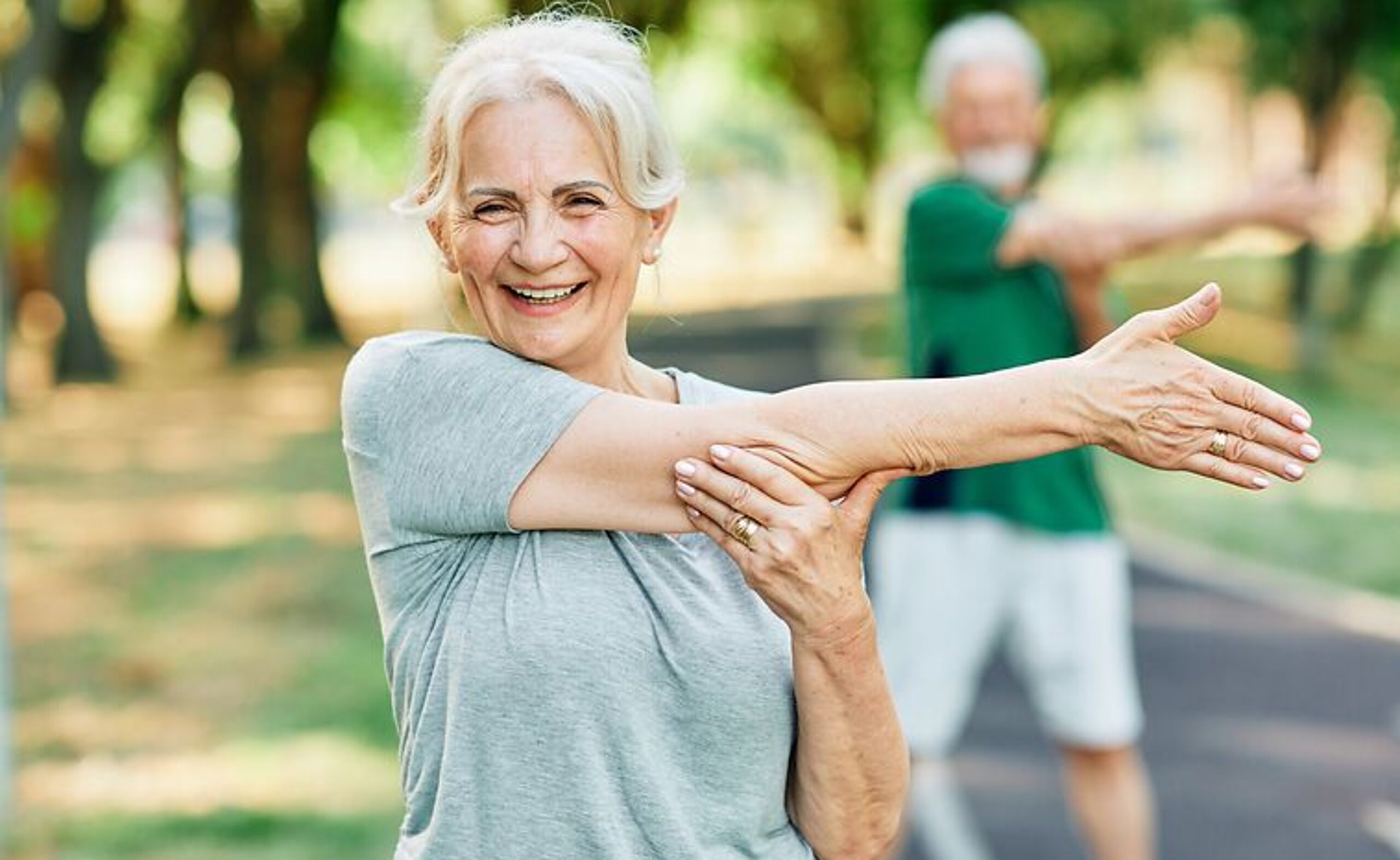 Patientin Gymnastik im Park Frau macht Arm-Dehnübungen im Park und lächelt dabei freundlich.