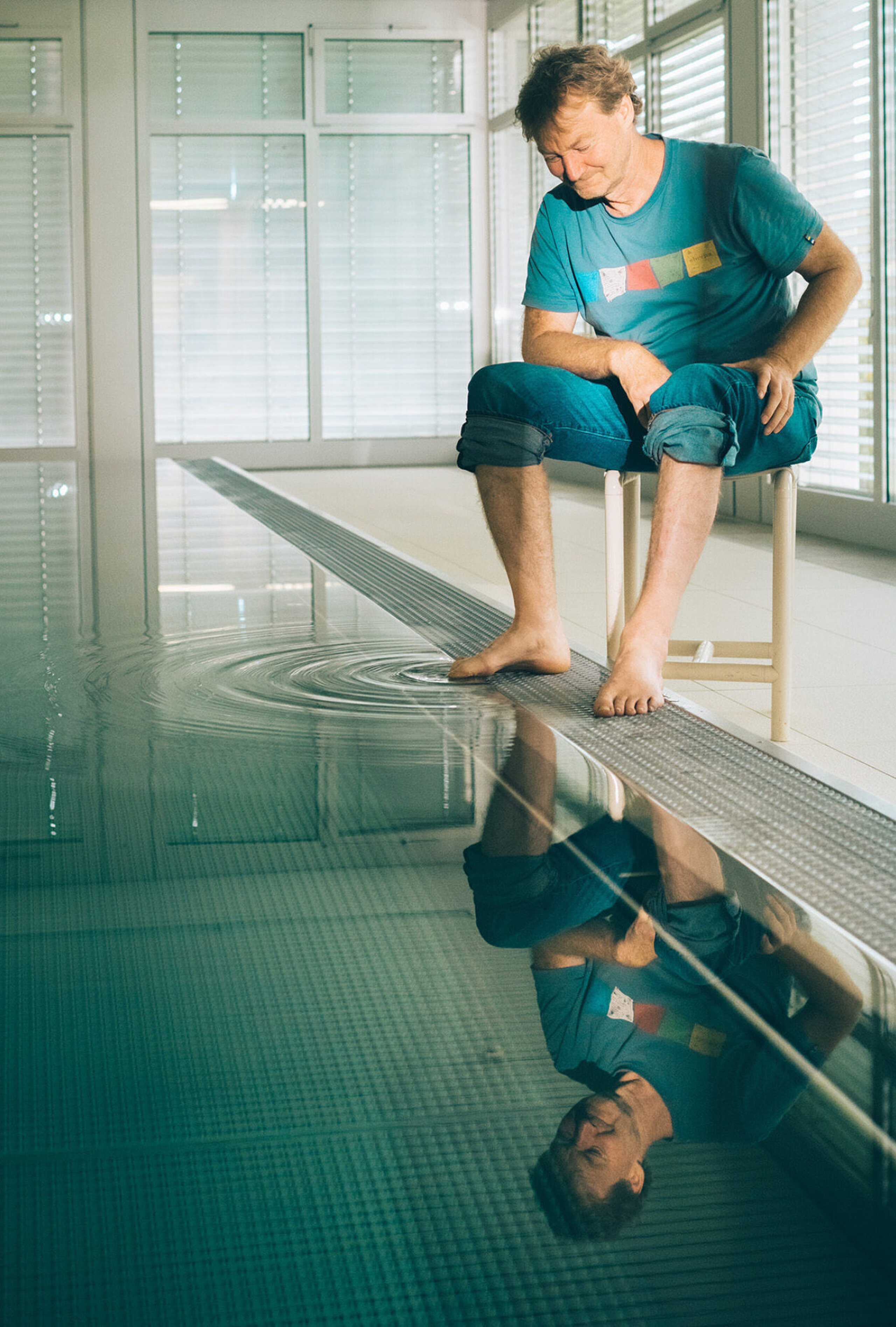 Thomas Lämmle sitzt am Rand des Bewegungsbades und streckt einen Zeh ins Wasser. 