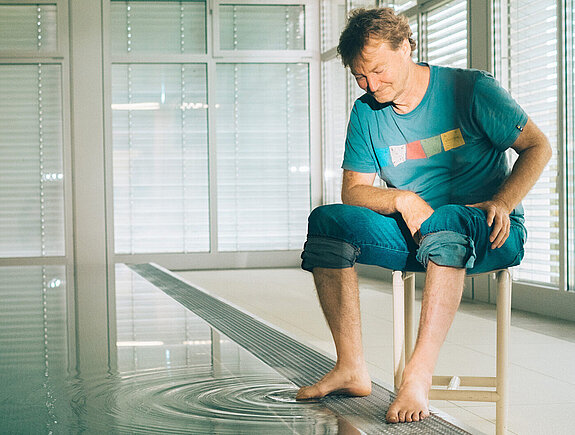 Thomas Lämmle sitzt am Rand des Bewegungsbades und streckt einen Zeh ins Wasser. 