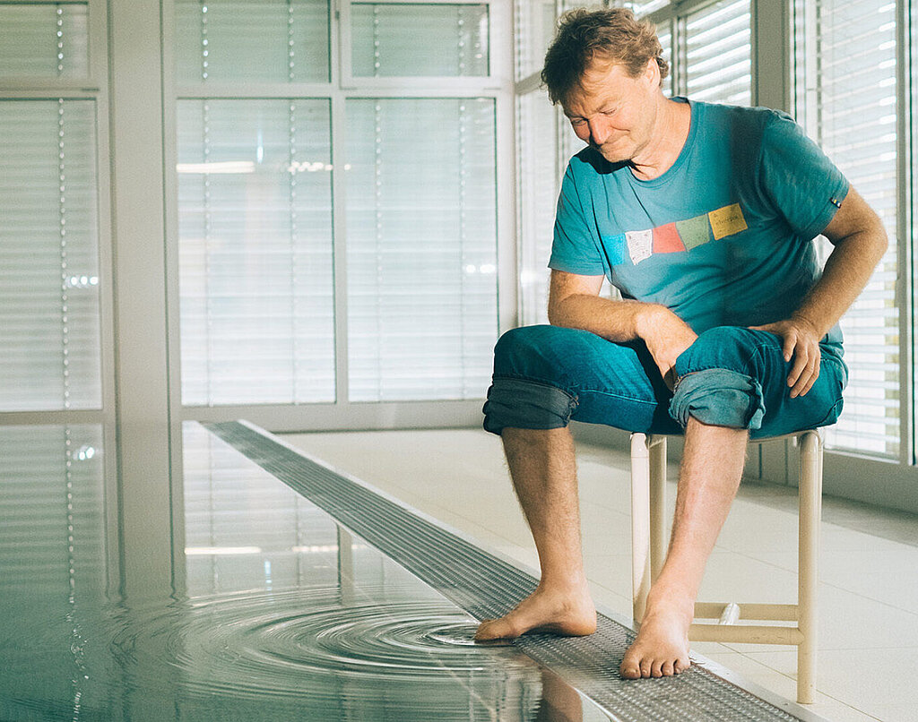 Thomas Lämmle sitzt am Rand des Bewegungsbades und streckt einen Zeh ins Wasser. 