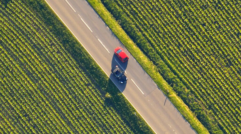 Luftaufnahme einer Landstraße mit zwei Autos, umgeben von grüner Landschaft.