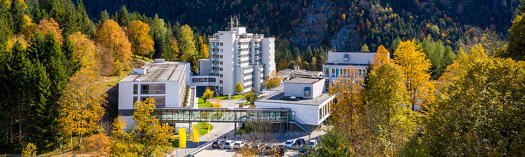 Klinik Oberammergau (Außenaufnahme) mitten im Herbstwald, im Hintergrund ist der Berg Laber zu sehen