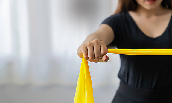Eine Frau hält ein Theraband mit ihrer Faust umschlossen.