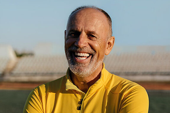 Ein Mann im Rentenalter lacht freundlich im Fußballstadion.