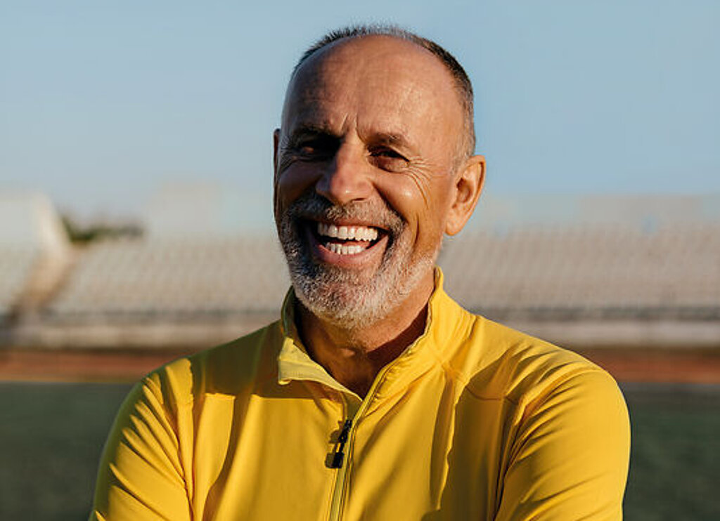 Ein Mann im Rentenalter lacht freundlich im Fußballstadion.