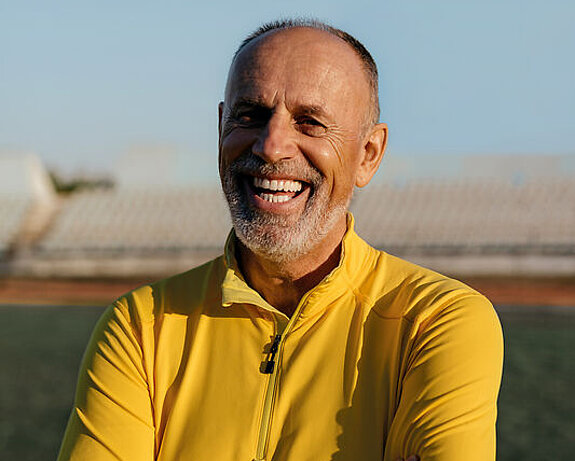 Ein Mann im Rentenalter lacht freundlich im Fußballstadion.