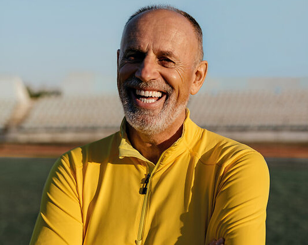 Ein Mann im Rentenalter lacht freundlich im Fußballstadion.