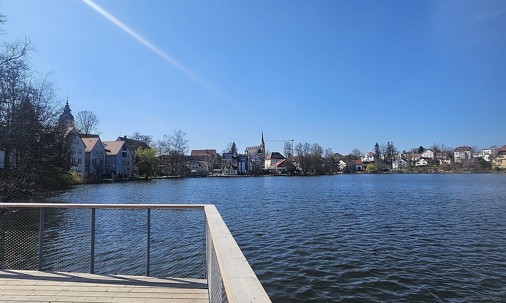 Holzsteg führt in den Stadtsee von Bad Waldsee, unter strahlend blauem Himmel.