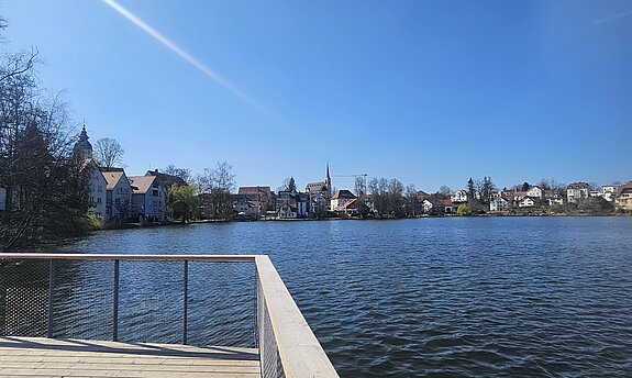 Holzsteg führt in den Stadtsee von Bad Waldsee, unter strahlend blauem Himmel.