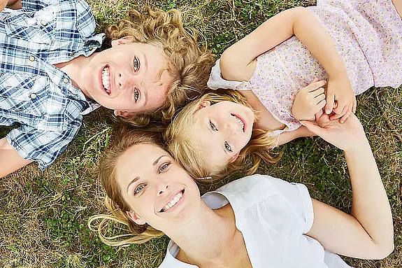 Mutter liegt mit Sohn und Tochter auf Wiese und schaut in den Himmel