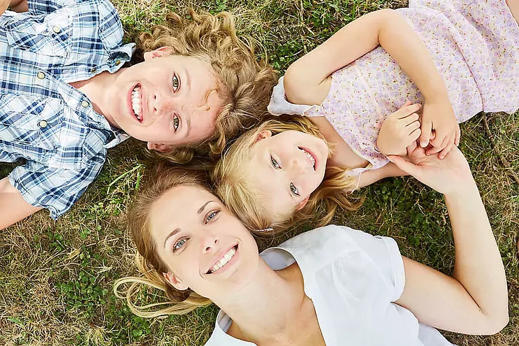 Mutter liegt mit Sohn und Tochter auf Wiese und schaut in den Himmel