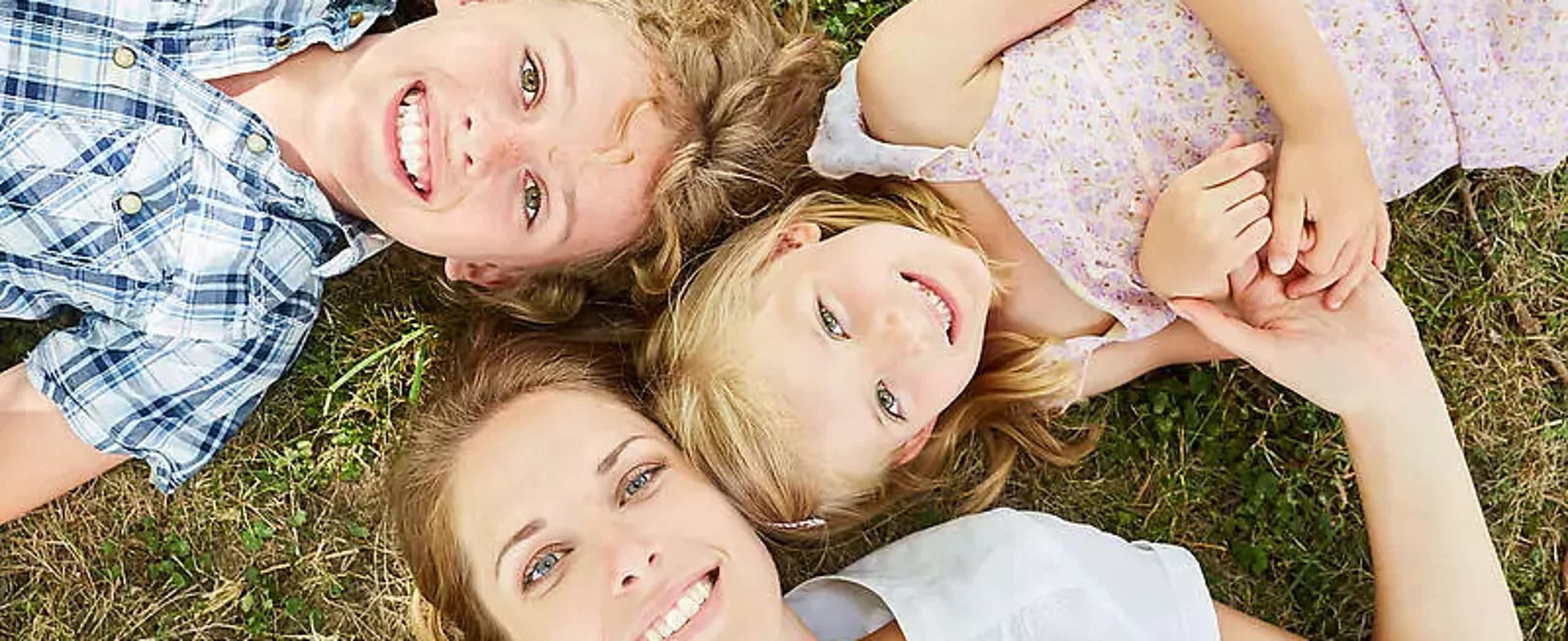 Mutter liegt mit Sohn und Tochter auf Wiese und schaut in den Himmel