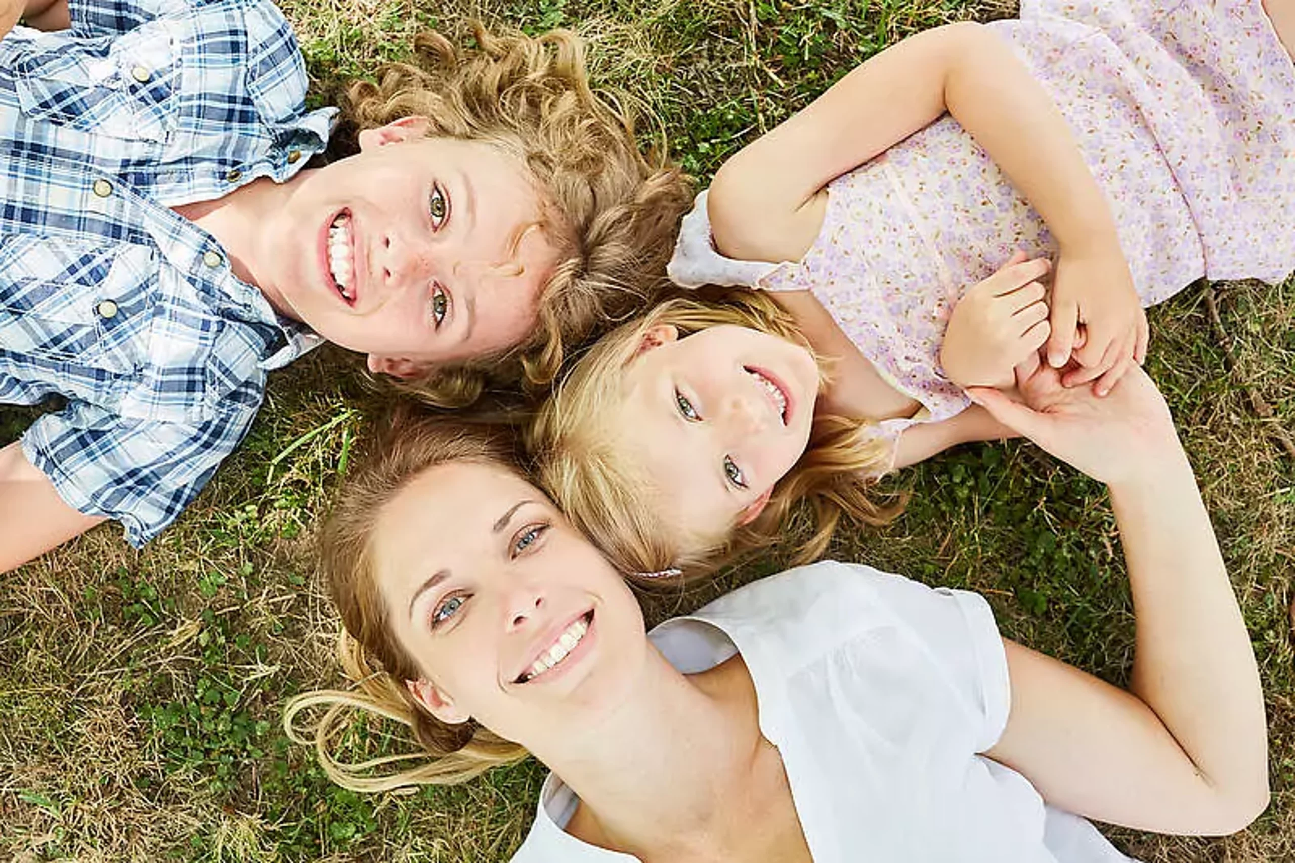 Mutter liegt mit Sohn und Tochter auf Wiese und schaut in den Himmel