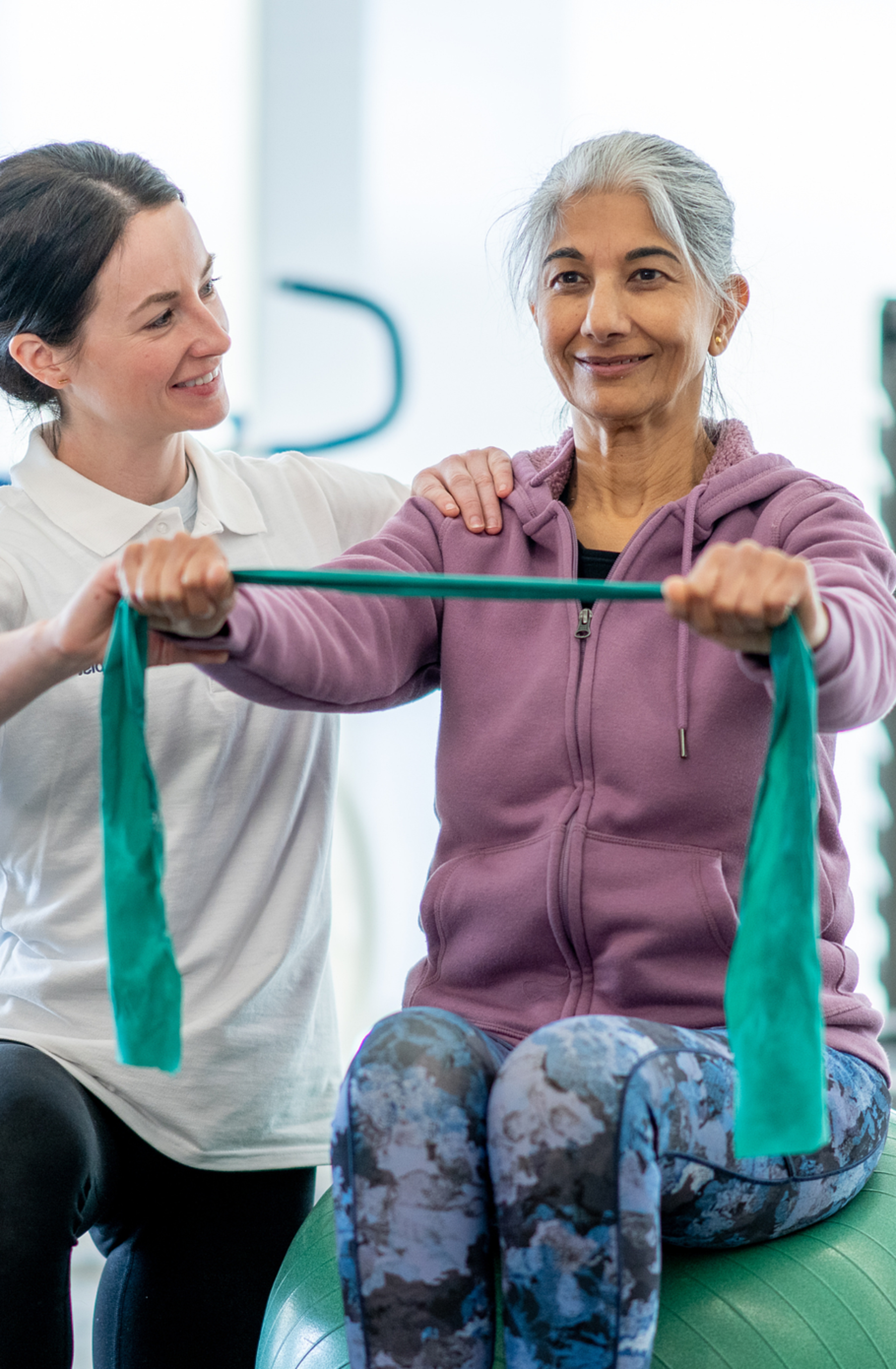 Eine Therapeutin unterstützt eine Patientin bei Übungen mit dem Therraband.