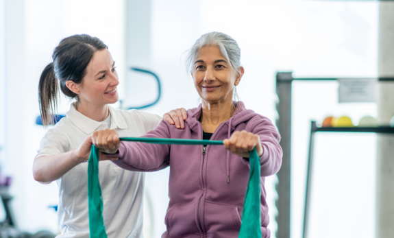 Eine Therapeutin unterstützt eine Patientin bei Übungen mit dem Therraband.