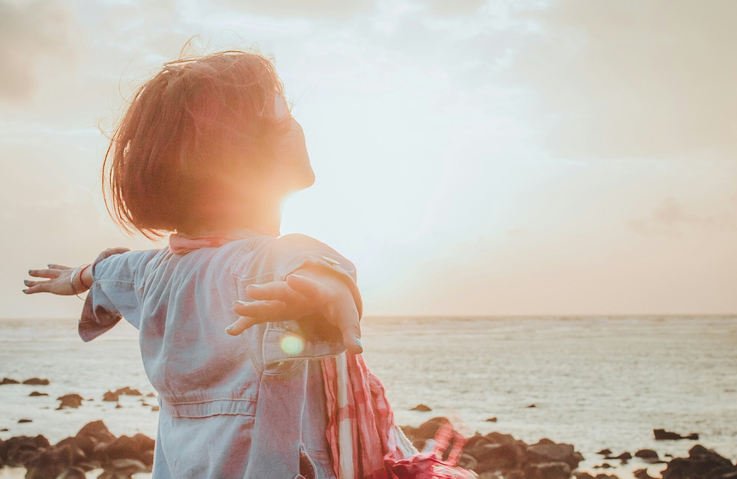 Eine Frau atmet tief ein mit ausgebreiteten Händen am Meer.
