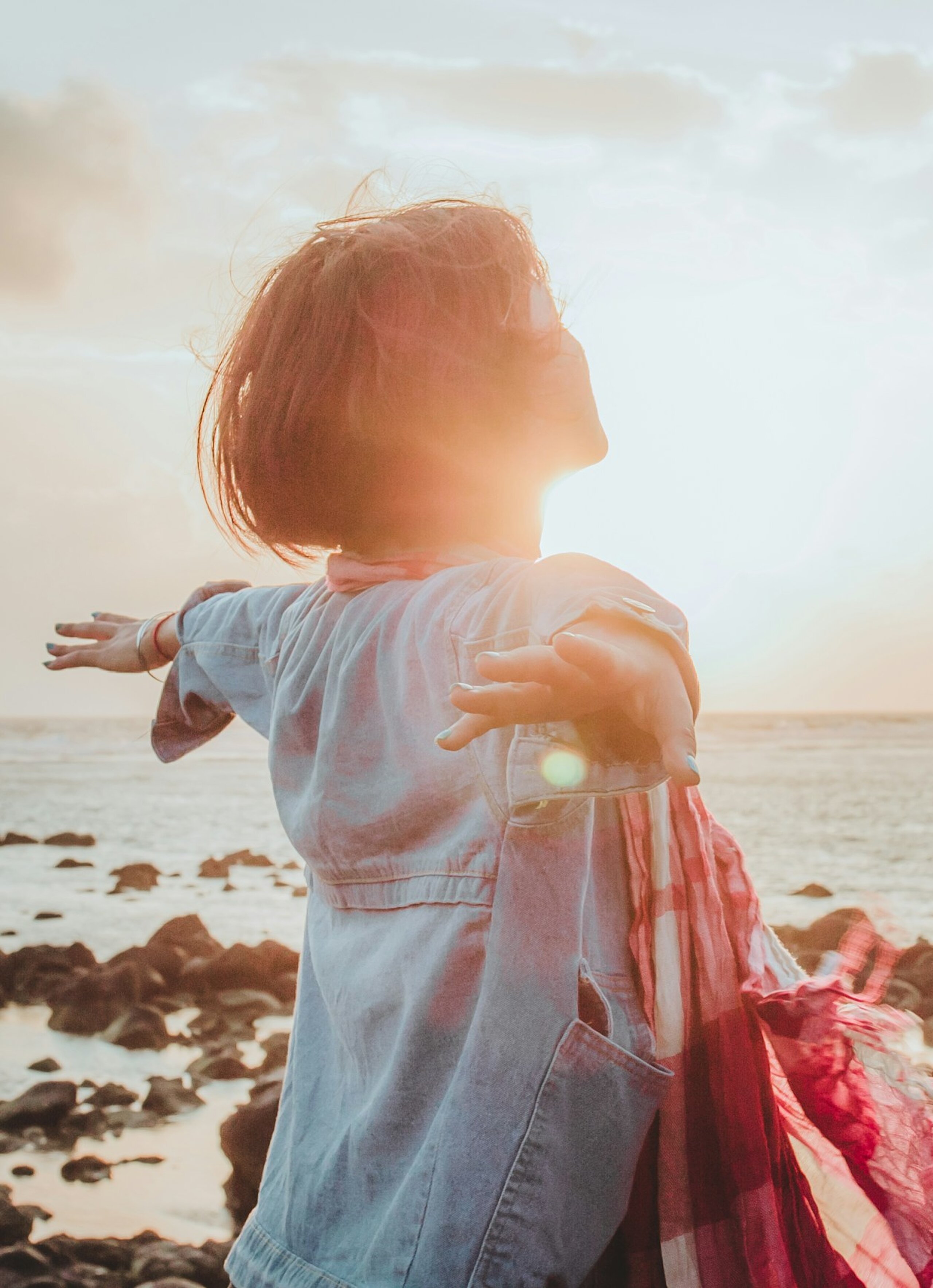 Eine Frau atmet tief ein mit ausgebreiteten Händen am Meer.