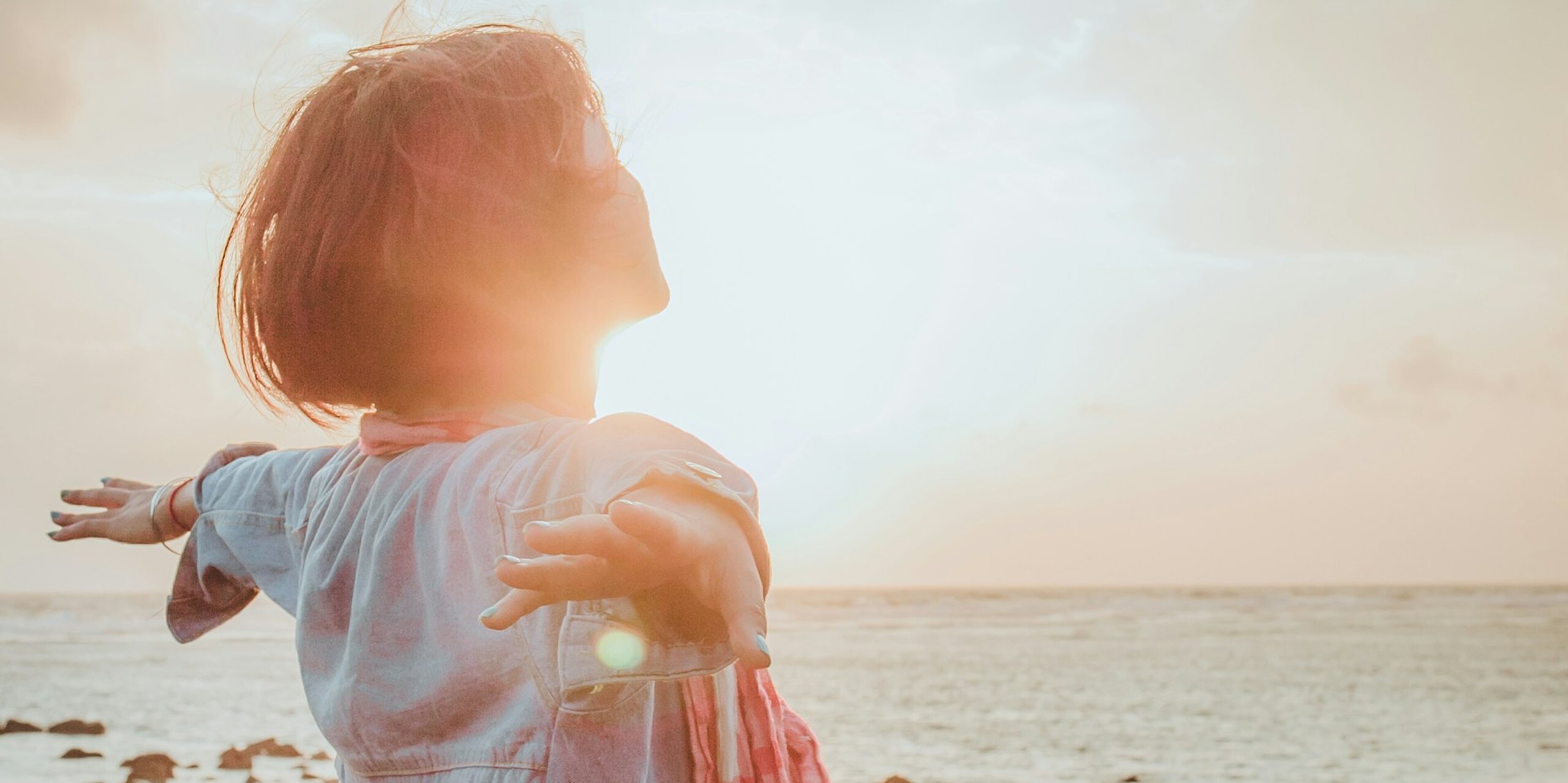 Eine Frau atmet tief ein mit ausgebreiteten Händen am Meer.