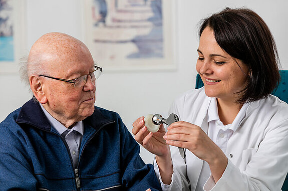 Eine Ärztin zeigt einem Patienten das Modell einer Hüftendoprothese.