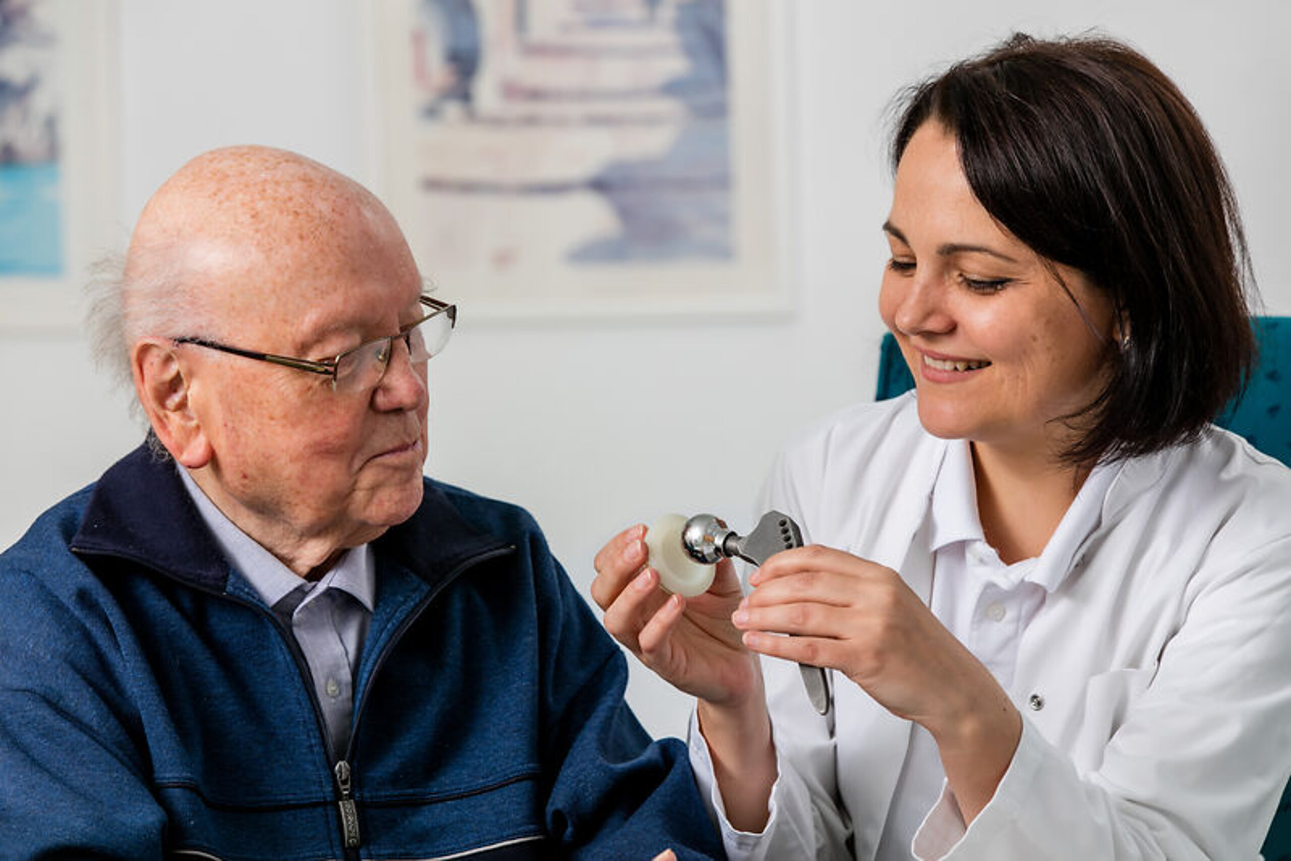 Eine Ärztin zeigt einem Patienten das Modell einer Hüftendoprothese.