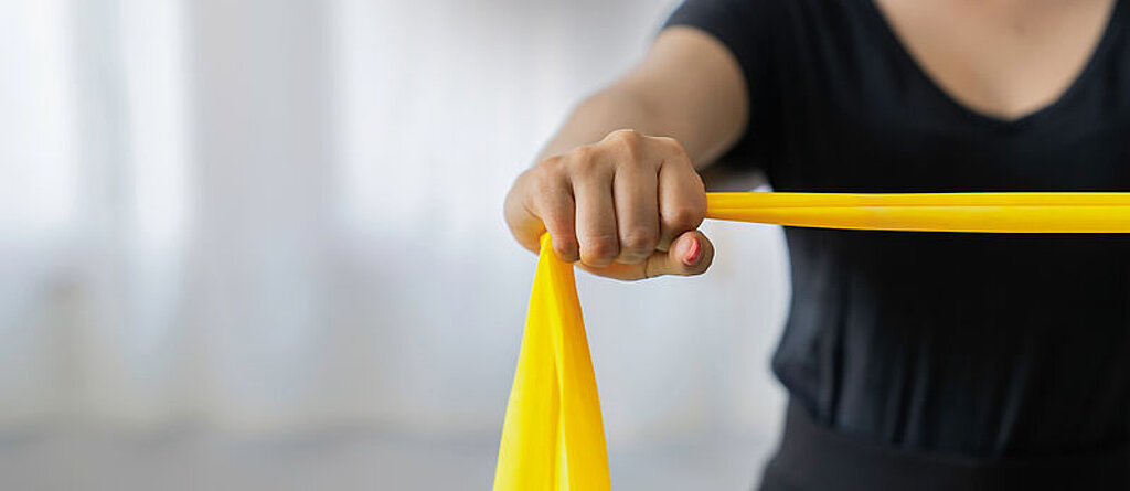 Eine Patientin macht Übungen mit einem gelben Therraband.