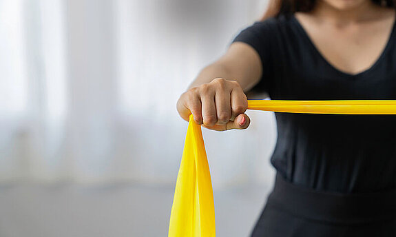 Eine Patientin macht Übungen mit einem gelben Therraband.