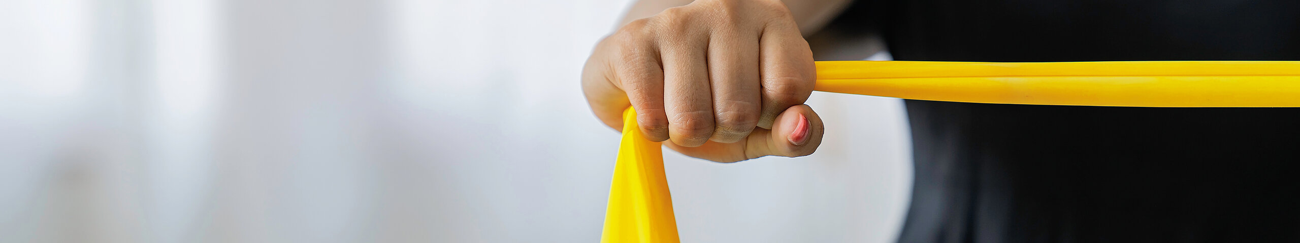 Eine Person hält ein gelbes Theraband und spannt es zur Stärkung der Armmuskulatur