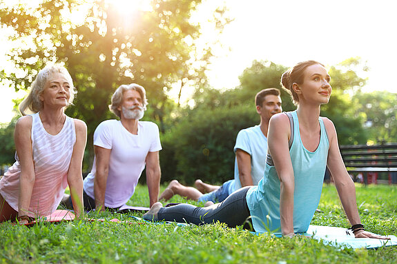 Eine Gruppe macht Dehnübungen auf einer Wiese.