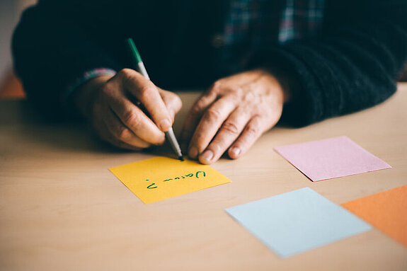Jemand schreibt innerhalb einer Psychotherapie etwas auf mehrere bunte Zettel.