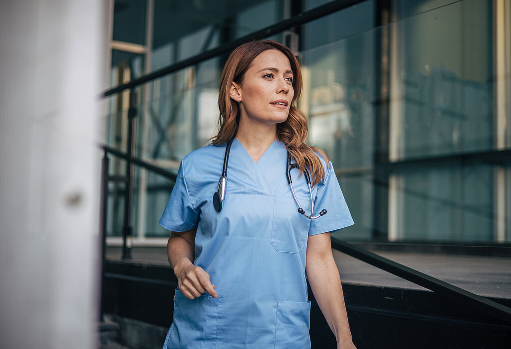 Eine Pflegekraft steht in einem Gang und schaut in die Ferne.