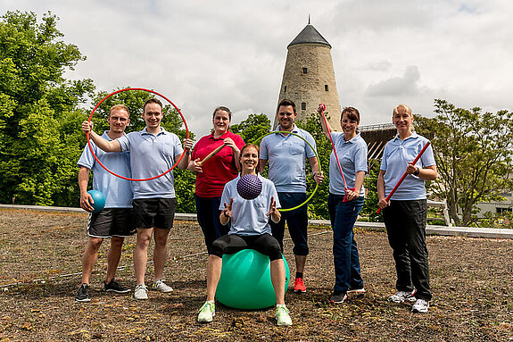 Team Therapie Eine Gruppe Therapeuten lächelt in die Kamera, mit Sportutensilien in den Händen.
