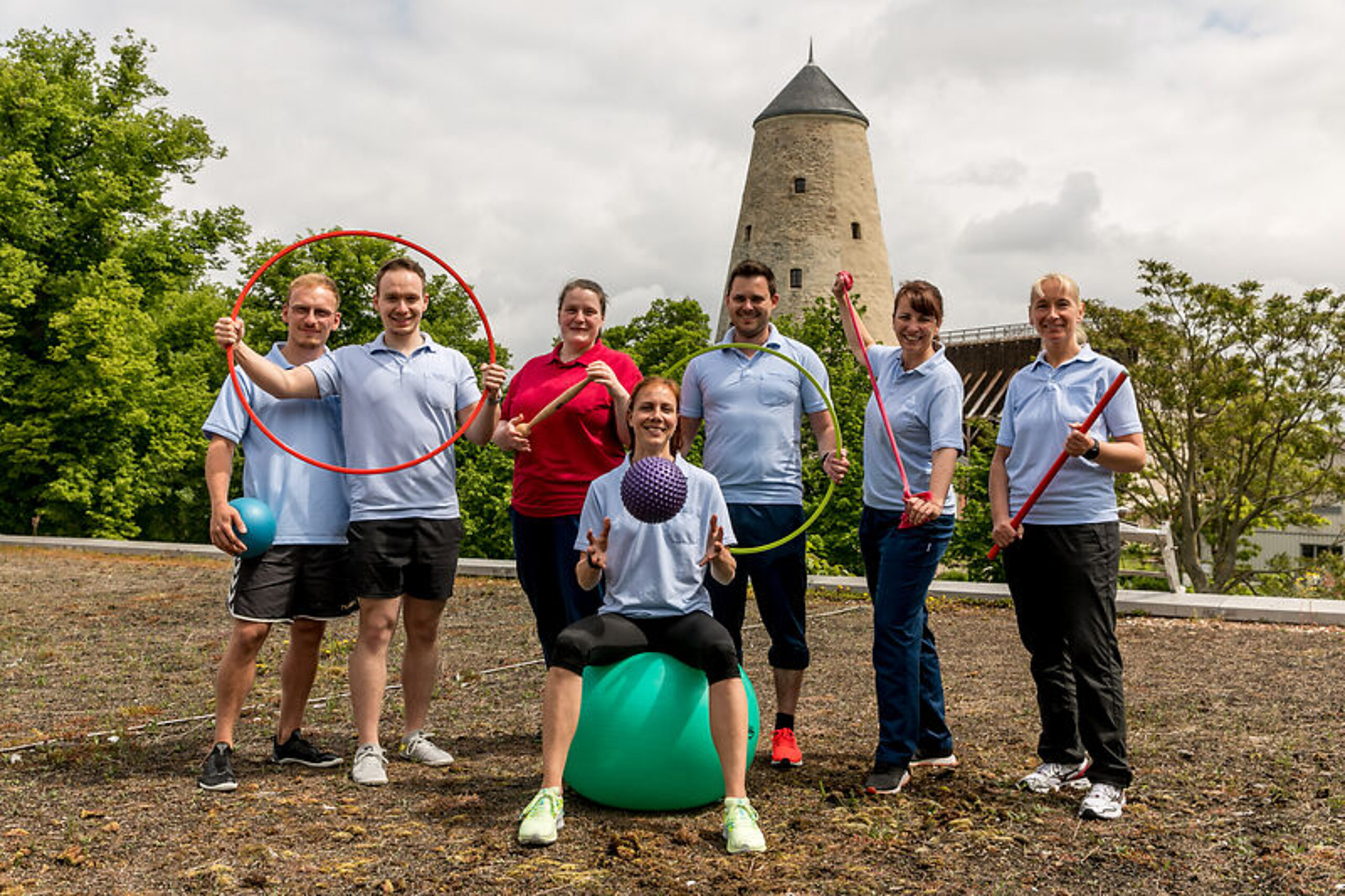 Team Therapie Eine Gruppe Therapeuten lächelt in die Kamera, mit Sportutensilien in den Händen.
