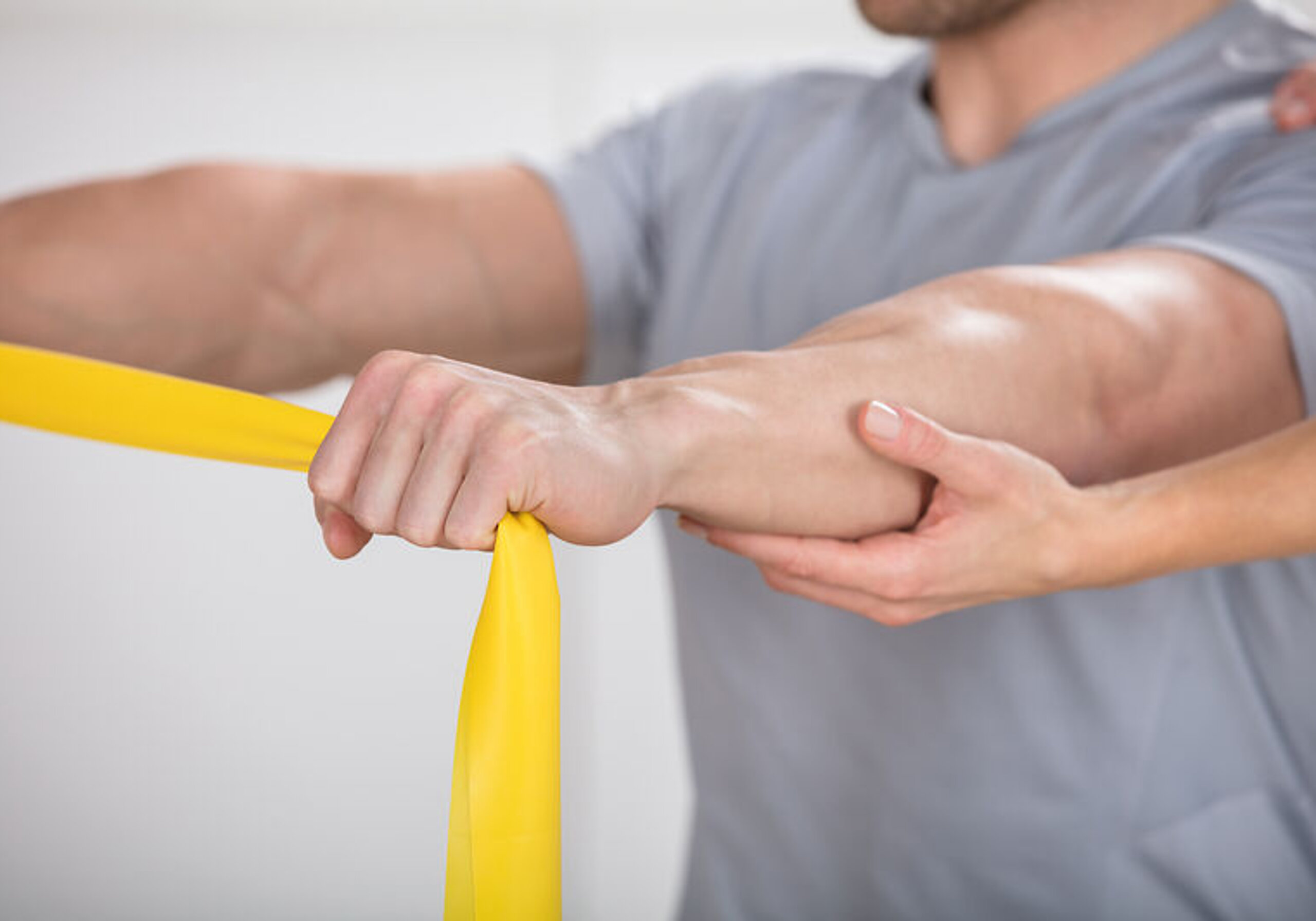 Ein Patient übt mit gelbem Terraband und wir dabei unterstützt.