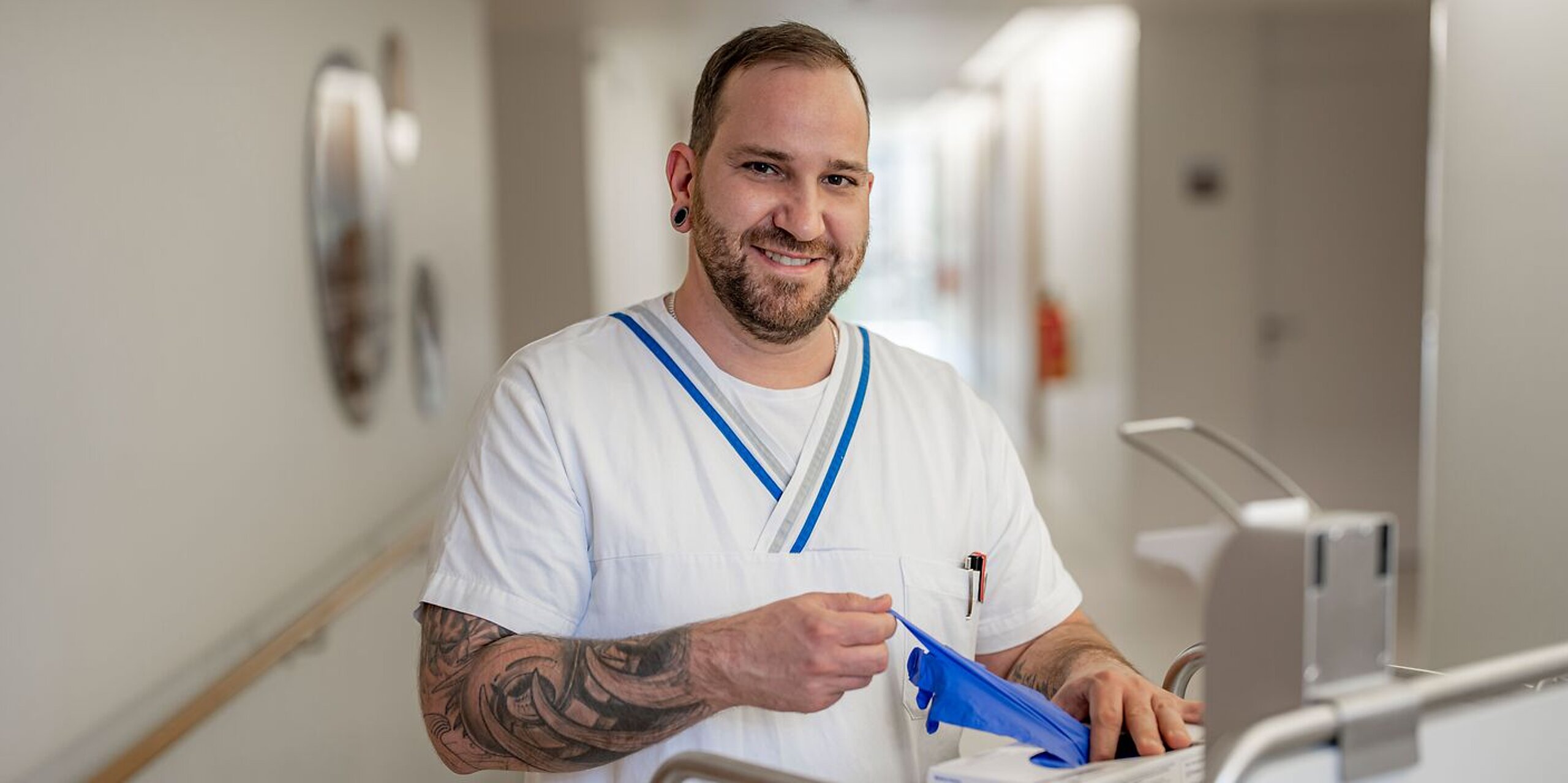 Ein freundlich lächelnder Pfleger zieht sich Einmalhandschuhe an.