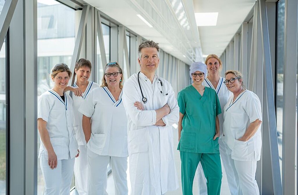 Arzt und ein Team aus Pflegekräften stehen gemeinsam in einem hellen Glasgang.