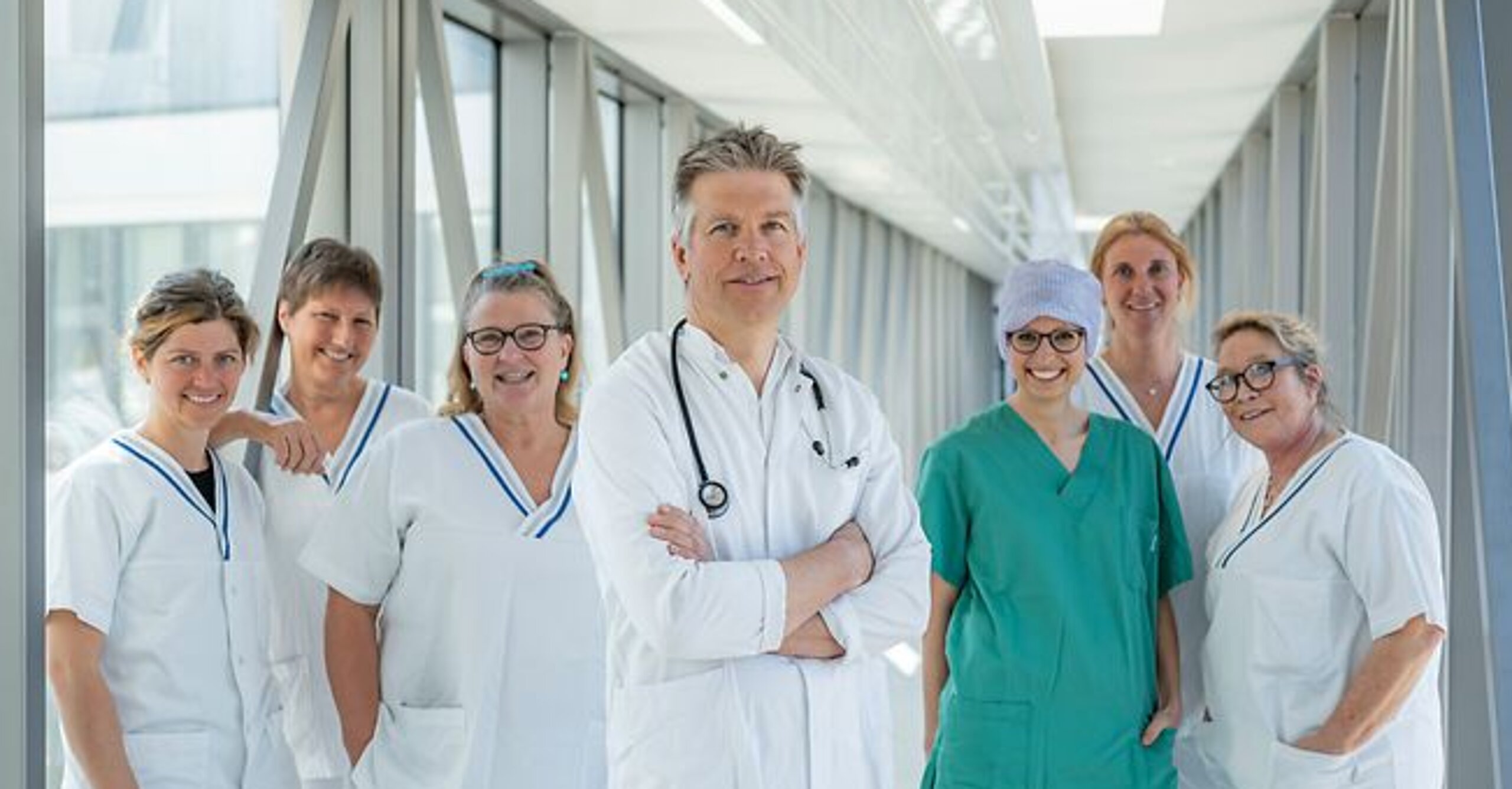 Arzt und ein Team aus Pflegekräften stehen gemeinsam in einem hellen Glasgang.