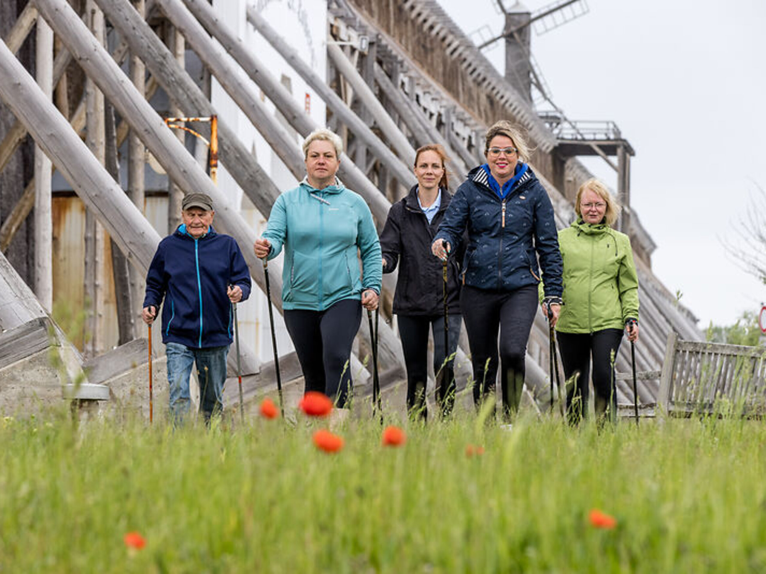 Fünf Personen laufen mit Walking-Stöcken in den Händen auf die Kamera zu, im Hintergrund befindet sich ein Gradierwerk.