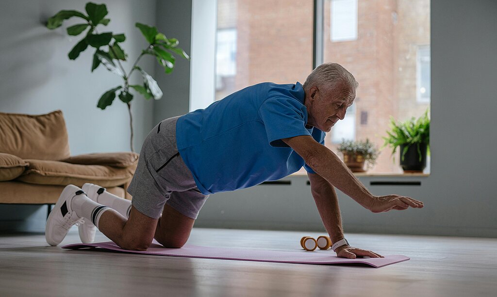 Ein älterer Mann macht zuhause auf einer Matte eine Stütz- und Mobilisationsübung für den Rücken