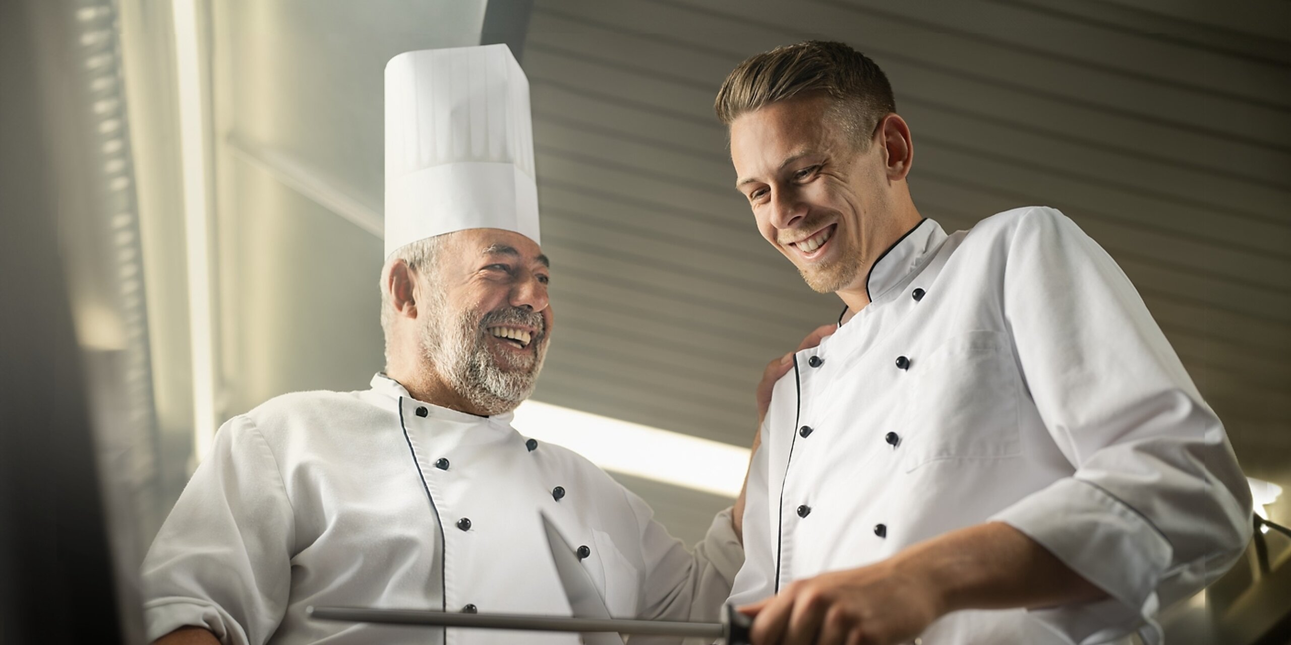 Ein alter Koch bringt einem jungen Koch etwas bei.