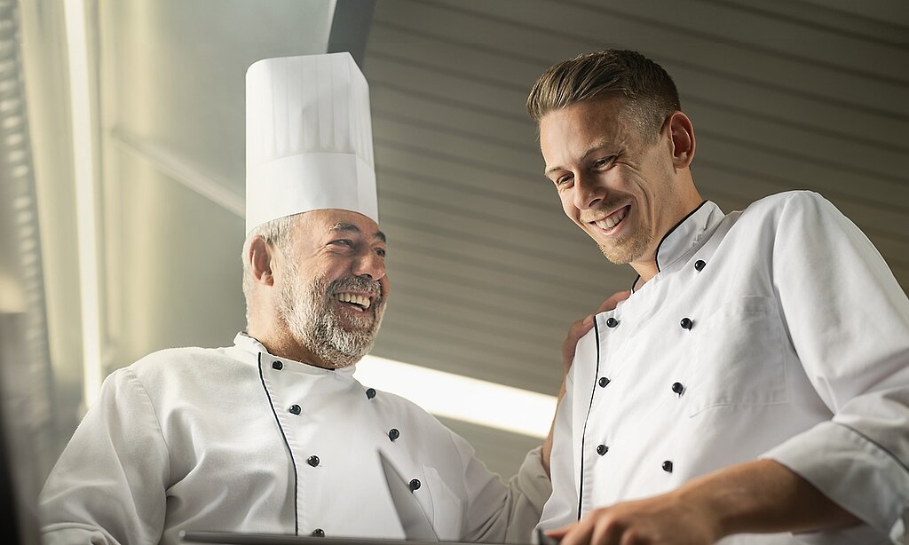 Ein alter Koch bringt einem jungen Koch etwas bei.