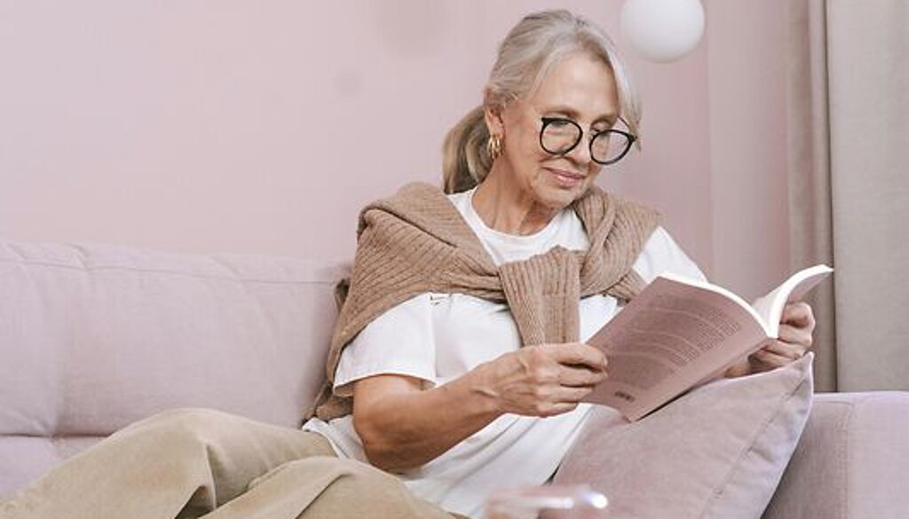 Eine Frau ließt zuhause ein Buch auf dem Sofa.