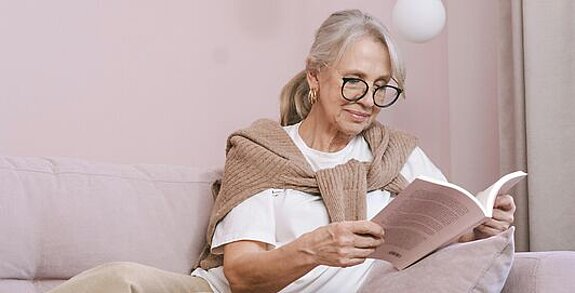 Eine Frau ließt zuhause ein Buch auf dem Sofa.