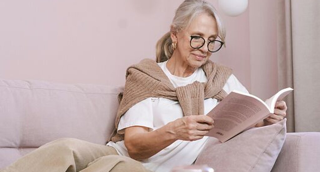 Eine Frau ließt zuhause ein Buch auf dem Sofa.