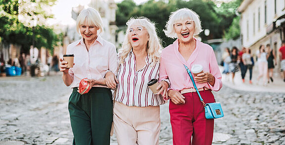 Seniorinnen Drei Seniorinnen laufen lachend durch die Straße.