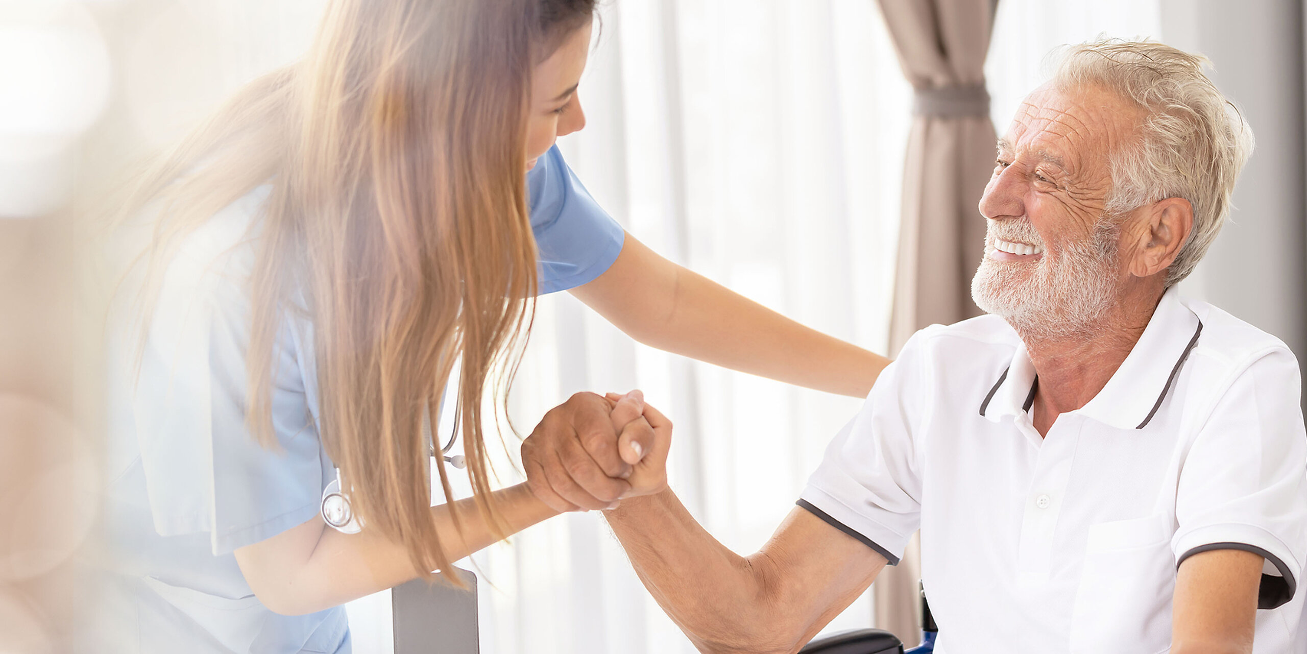 Eine freundliche Pflegerin betreut einen älteren Mann im Rollstuhl.