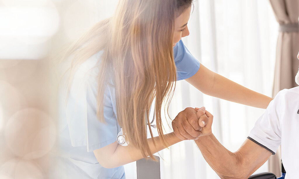 Eine freundliche Pflegerin betreut einen älteren Mann im Rollstuhl.