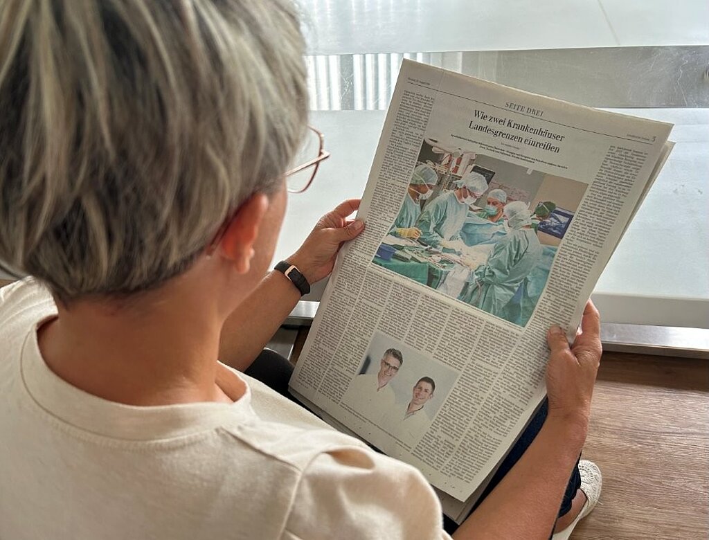 Frau liest in der Schwäbischen Zeitung vom 25. August 2026 den Artikel „Wie zwei Krankenhäuser Landesgrenzen einreißen“.